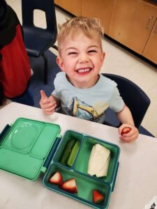 un élève sourit assis devant sa lunch box